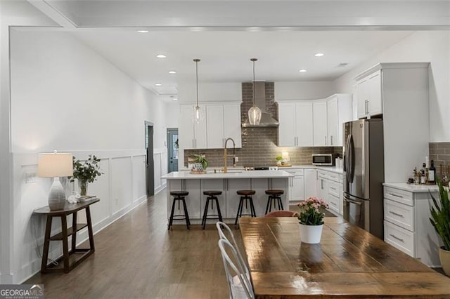 kitchen with stainless steel appliances, light countertops, a center island with sink, and wall chimney range hood