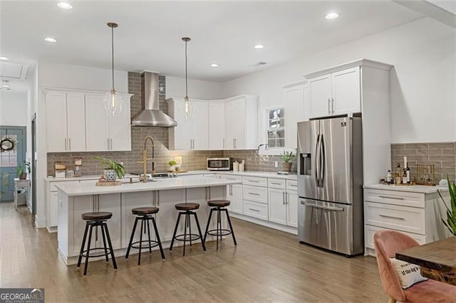 kitchen with wall chimney exhaust hood, appliances with stainless steel finishes, light countertops, white cabinetry, and pendant lighting