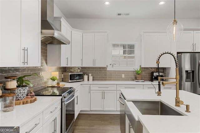 kitchen featuring appliances with stainless steel finishes, white cabinets, light countertops, and wall chimney exhaust hood