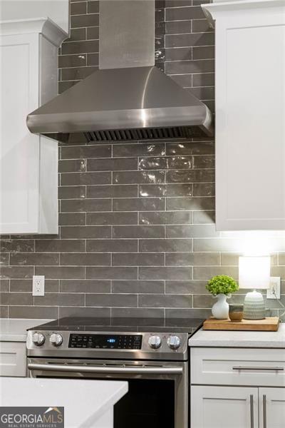 kitchen featuring electric range, white cabinetry, light countertops, wall chimney range hood, and backsplash