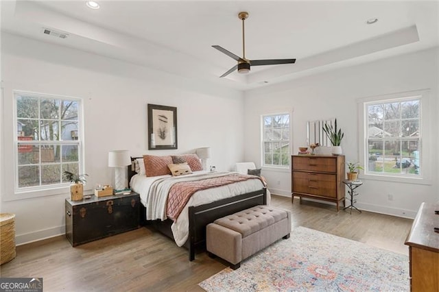 bedroom featuring a tray ceiling, visible vents, baseboards, and wood finished floors