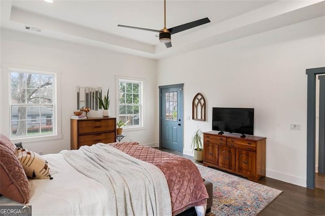 bedroom featuring dark wood-style floors, baseboards, visible vents, and a tray ceiling