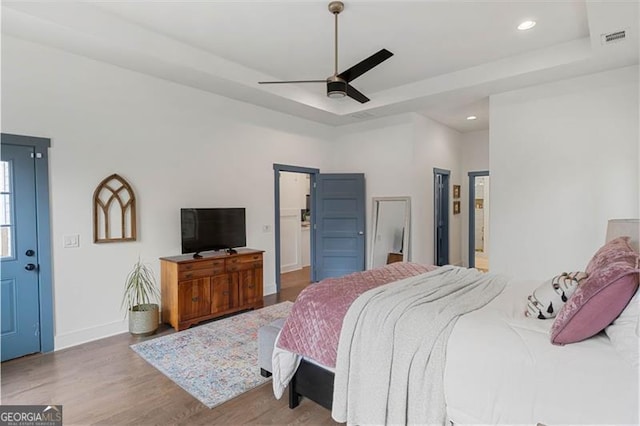 bedroom with a tray ceiling, wood finished floors, visible vents, and recessed lighting