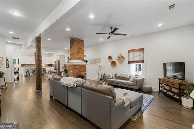 living area featuring dark wood-style flooring, recessed lighting, visible vents, a brick fireplace, and baseboards