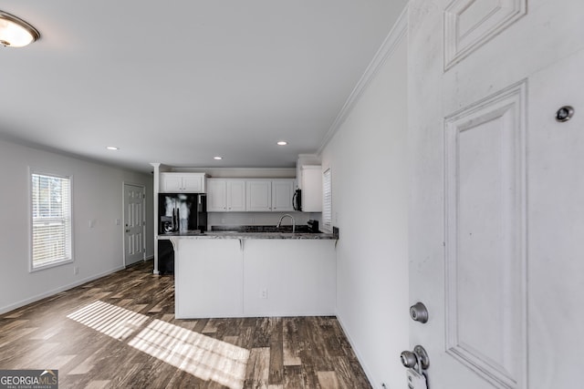 kitchen with kitchen peninsula, black appliances, ornamental molding, dark wood-type flooring, and white cabinets