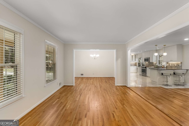 unfurnished living room featuring light wood-style flooring, ornamental molding, and a notable chandelier