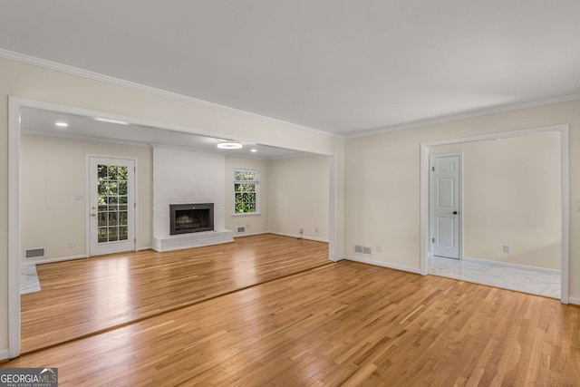 unfurnished living room featuring ornamental molding, light wood finished floors, a brick fireplace, and visible vents