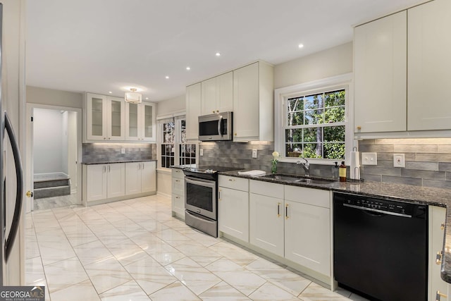 kitchen with appliances with stainless steel finishes, white cabinetry, a sink, and dark stone countertops