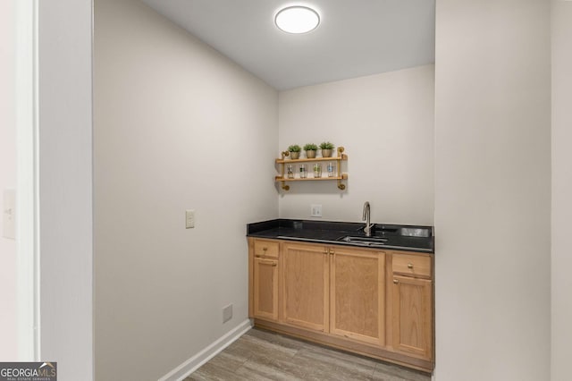 bar with a sink, light wood-style flooring, and baseboards