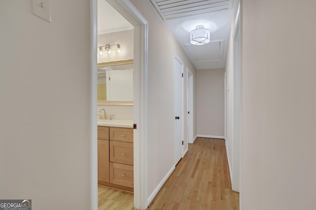 corridor featuring attic access, a sink, light wood-style flooring, and baseboards