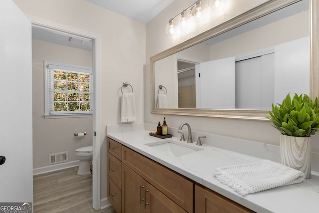 full bath with baseboards, visible vents, toilet, wood finished floors, and vanity