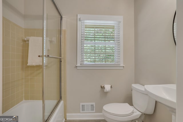 full bath featuring toilet, shower / bath combination with glass door, a sink, visible vents, and baseboards