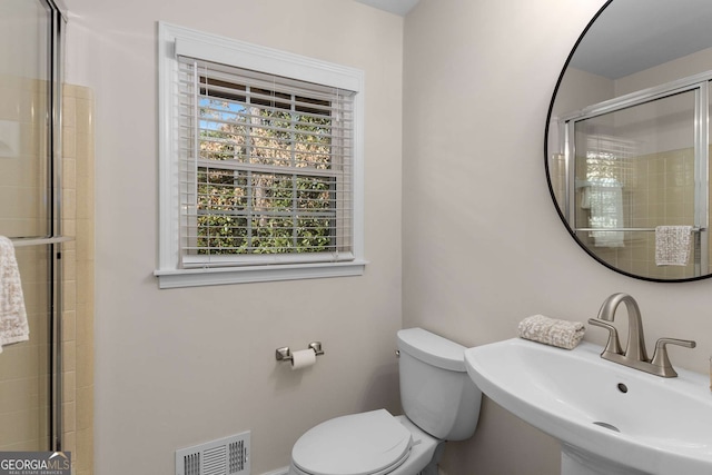 bathroom featuring toilet, a shower with shower door, a sink, and visible vents