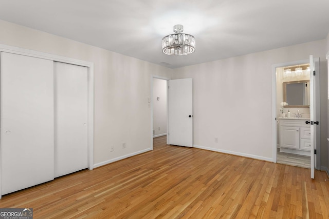 unfurnished bedroom with a notable chandelier, ensuite bathroom, light wood-style floors, a sink, and baseboards