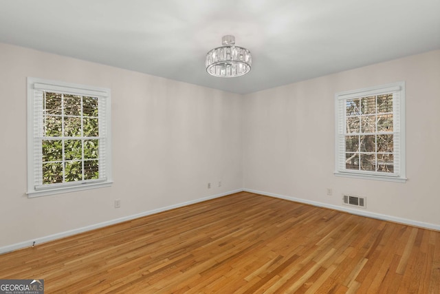 spare room with a notable chandelier, wood finished floors, visible vents, and baseboards