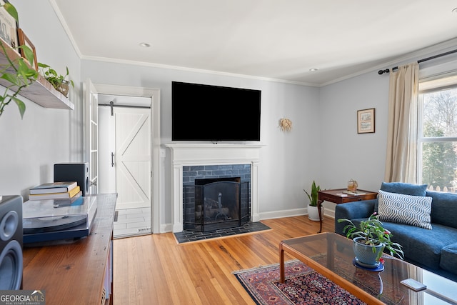 living area featuring a barn door, a fireplace, wood finished floors, baseboards, and ornamental molding