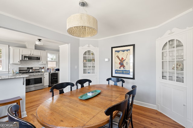 dining room with wine cooler, baseboards, crown molding, and light wood finished floors