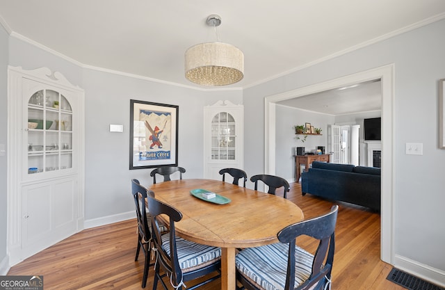 dining space with baseboards, visible vents, ornamental molding, light wood-style floors, and a fireplace