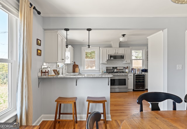 kitchen featuring wine cooler, stainless steel appliances, a peninsula, white cabinetry, and hanging light fixtures