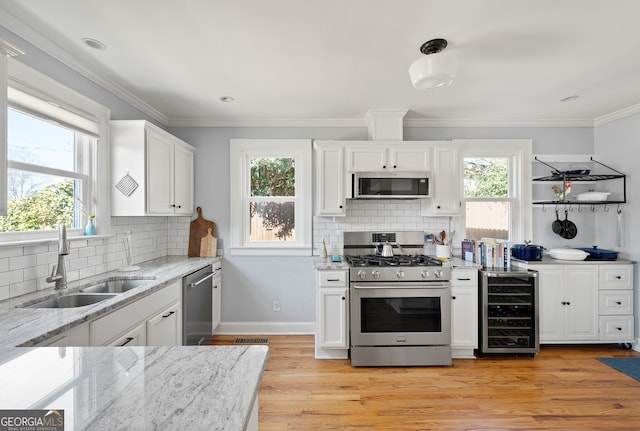 kitchen with beverage cooler, stainless steel appliances, a sink, and white cabinets