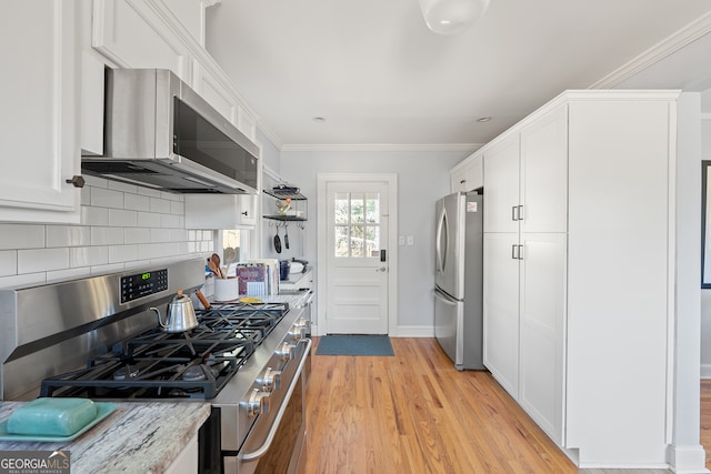 kitchen with light stone counters, stainless steel appliances, white cabinetry, light wood-type flooring, and backsplash