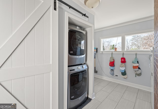 washroom featuring stacked washer and dryer, a barn door, laundry area, and baseboards