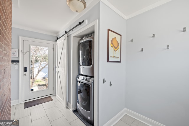 laundry area featuring laundry area, a barn door, baseboards, ornamental molding, and stacked washer / drying machine