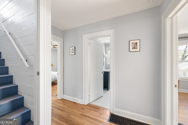 corridor with stairs, crown molding, baseboards, and light wood-style floors