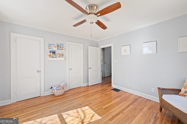 sitting room with a ceiling fan, baseboards, visible vents, light wood finished floors, and crown molding