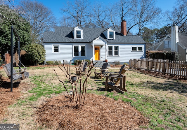 rear view of house featuring a yard, roof with shingles, a chimney, and fence