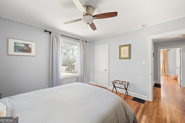 bedroom with light wood finished floors, visible vents, baseboards, and ornamental molding