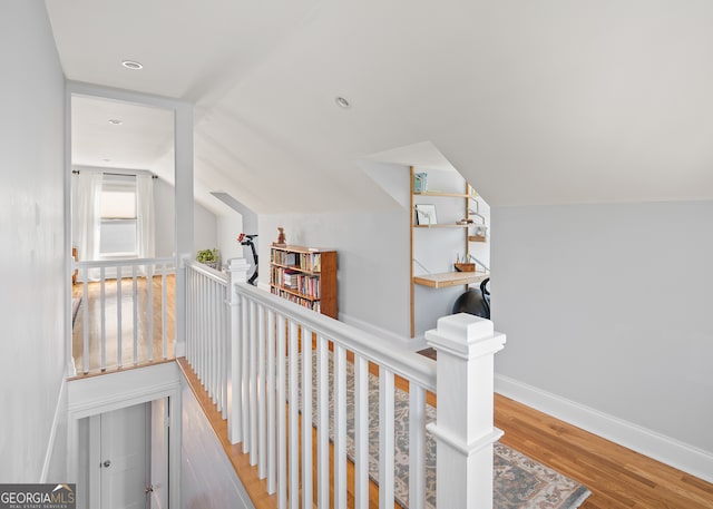 hallway with vaulted ceiling, wood finished floors, an upstairs landing, and baseboards