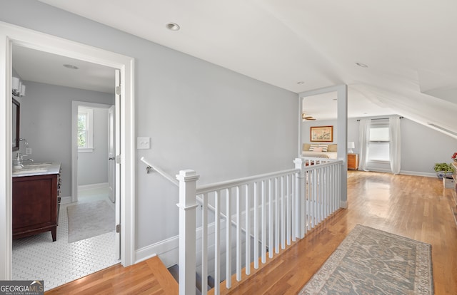 hallway with light wood-style flooring, baseboards, a sink, and an upstairs landing