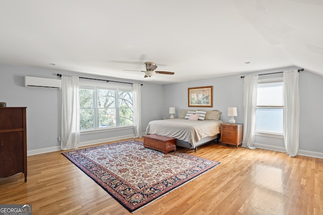 bedroom with light wood finished floors, multiple windows, baseboards, and a wall mounted AC