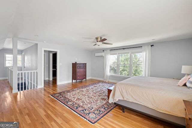 bedroom featuring a ceiling fan, a wall unit AC, baseboards, and wood finished floors