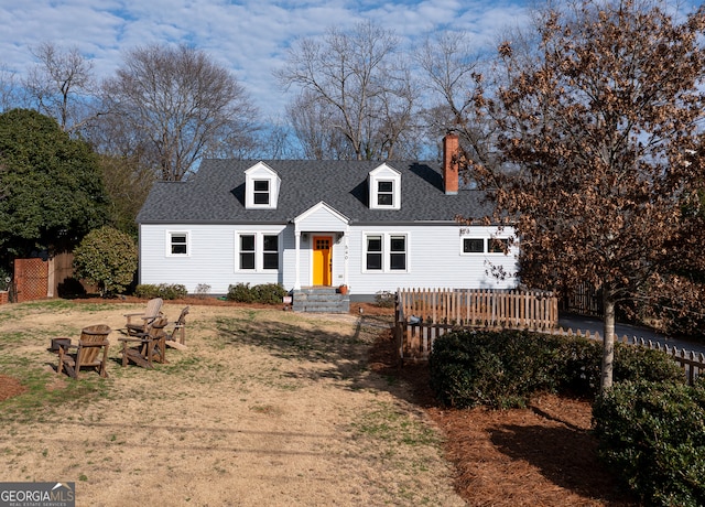 new england style home featuring entry steps, a chimney, a front lawn, and roof with shingles