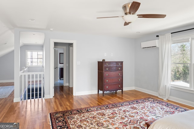 bedroom with a wall mounted air conditioner, vaulted ceiling, baseboards, and wood finished floors