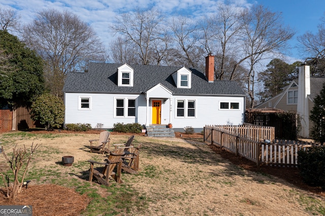 view of front facade featuring a shingled roof, a chimney, fence, and a front yard