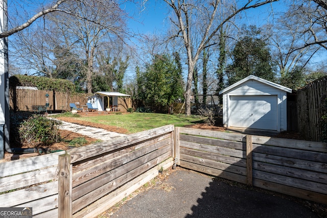 view of yard featuring a garage, a fenced backyard, an outdoor structure, and driveway