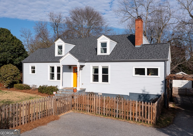 cape cod-style house featuring a fenced front yard, roof with shingles, and a chimney