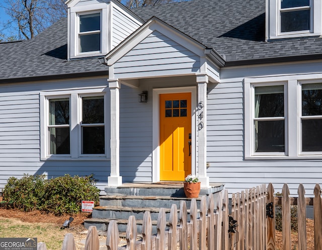 entrance to property featuring a shingled roof and fence