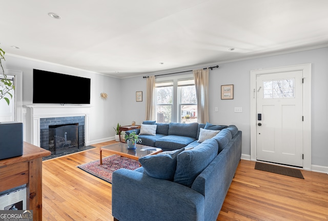 living area with baseboards, a fireplace with flush hearth, ornamental molding, and wood finished floors