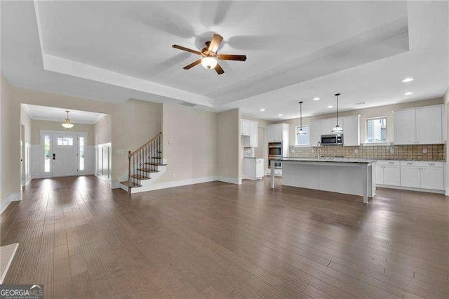unfurnished living room featuring ceiling fan, a wealth of natural light, a raised ceiling, and dark wood finished floors