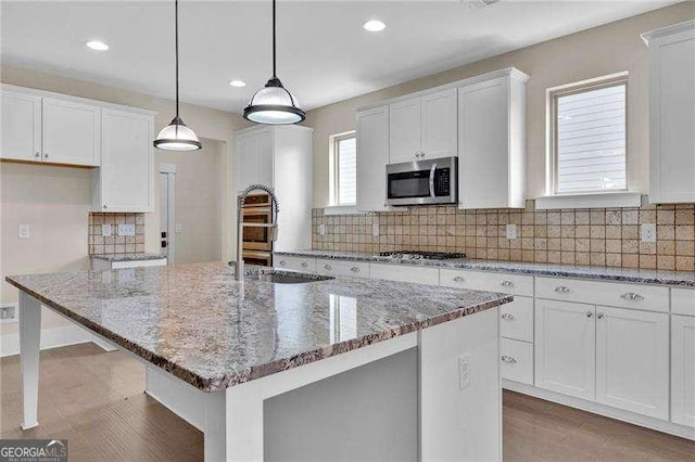 kitchen featuring white cabinetry, a center island, stainless steel appliances, and light stone countertops
