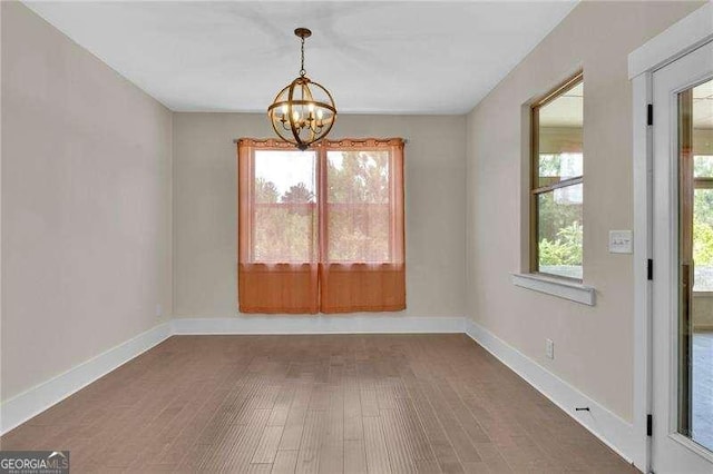 unfurnished dining area featuring an inviting chandelier, wood finished floors, and baseboards