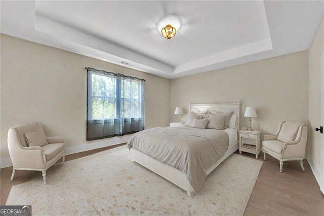 bedroom featuring baseboards, a raised ceiling, and wood finished floors