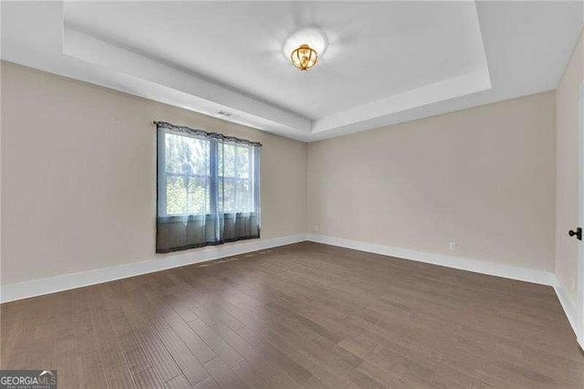empty room with wood finished floors, a tray ceiling, and baseboards