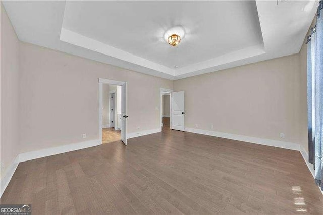 empty room featuring wood finished floors, a tray ceiling, and baseboards