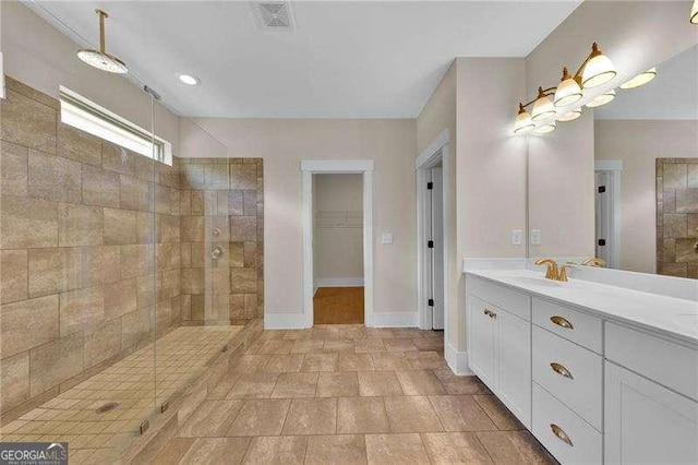 bathroom with baseboards, visible vents, tiled shower, and vanity