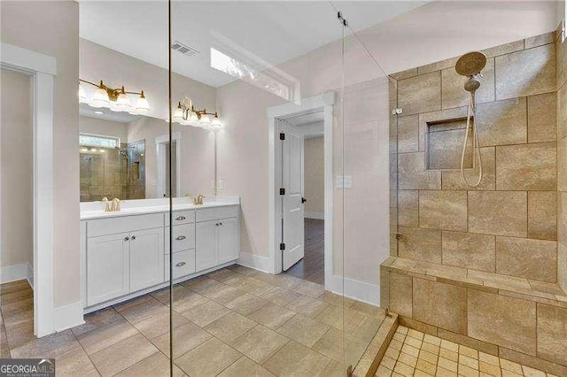 full bath with double vanity, baseboards, tiled shower, and a sink